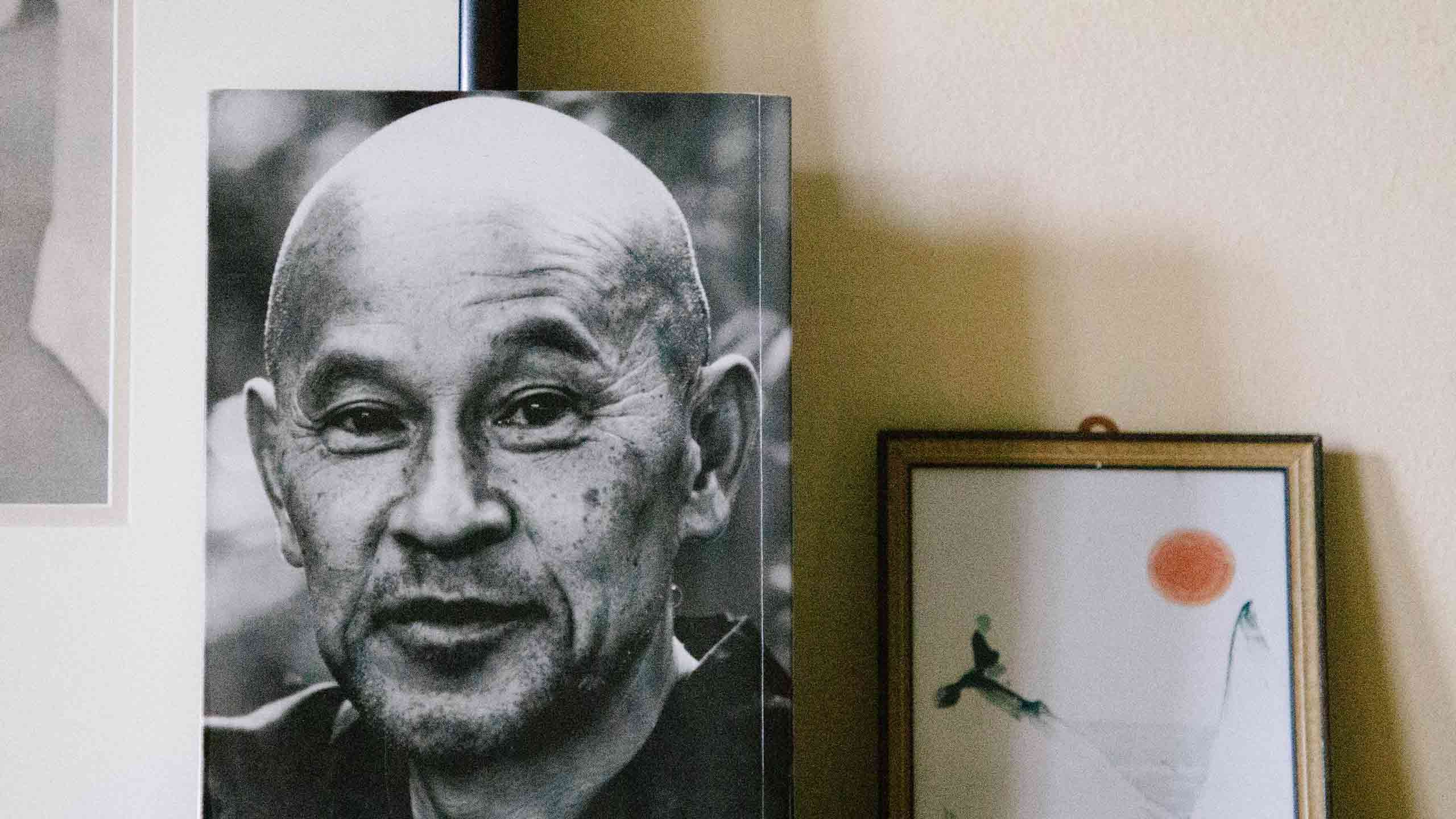 Buchcover Zen Geist Anfänger Geist mit dem Kopf von Shunryu Suzuki Roshi neben einem Bild an die Wand gelehnt